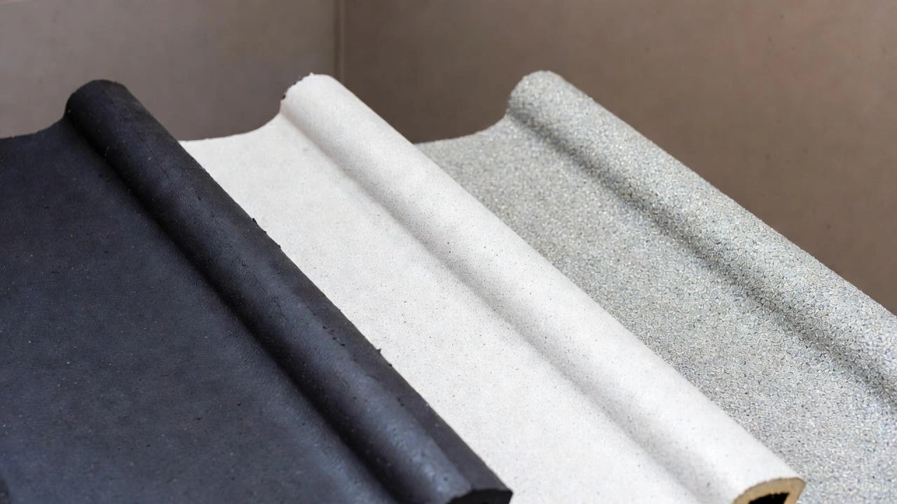 Rolled samples of various types of rubber roofing membranes, including black (EPDM), white (TPO/PVC), and a granular-coated white or gray material.