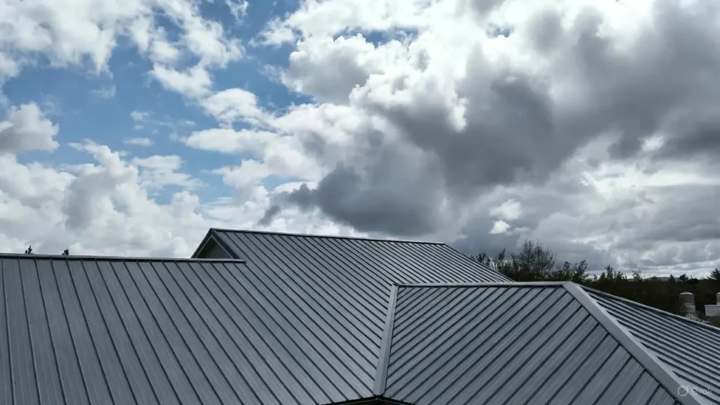 A wide-angle view of a professionally installed gray standing seam metal roof with clean vertical ribs under a dramatic cloudy sky