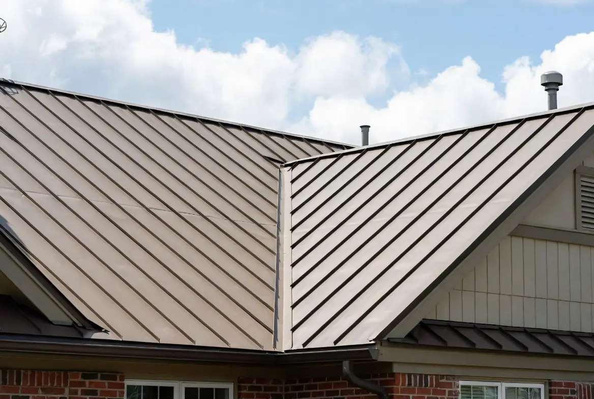 A close-up view of a professionally installed bronze standing seam aluminum roof featuring clean vertical ribs, concealed fasteners, and a durable matte finish on a brick-accented home.